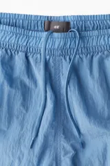 Short de baño azul de nylon con elástico revestido y cordón para ajustar oculto en la cintura, bolsillos laterales y bolsillo de solapa con cierre autoadherente atrás. Largo por encima de la rodilla con abertura corta en los laterales y suspensor interior en malla suave.