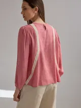 Camisa celeste de algodón con detalle de encaje blanco en el frente. Tiene mangas largas abullonadas con puños anchos y cuello redondo.