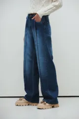 Pantalón de jean azul de corte recto y amplio, con tablas marcadas al frente y lavado azul con fuertes localizados.