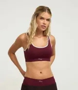 Top deportivo tipo bralette color bordó, sin aros ni copas, con ribetes blancos en el escote y la sisa. Presenta un tejido texturizado y el logo de la marca bordado en la banda inferior.