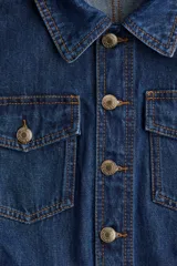 Mono corto de denim azul, con cuello camisero, cierre frontal con botones, mangas cortas, bolsillos superiores de parche con botón, bolsillos al bies y bolsillos insertados atrás. Incluye cinturón extraíble para atar en la cintura.
