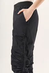 Pantalón jogger negro de nylon con elástico ancho en la cintura, puños elásticos ajustables y lazos laterales para fruncir.