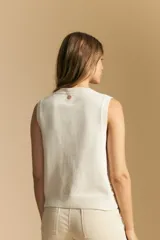 Chaleco tejido sin mangas color blanco roto, con cuello redondo y cartera frontal de botones. Presenta un punto calado con textura.