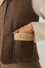 Chaleco corto color beige, de corte recto y abierto, con cuello de piel sintética blanca y apliques de cuero marrón en los bolsillos.