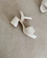 Sandalia de tacón blanco, elaborada en 100% cuero vacuno, con diseño abierto y tira cruzada.