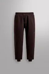 Pantalón jogger color marrón oscuro, corte regular fit, confeccionado en tejido técnico compacto de algodón con elasticidad. Cuenta con cintura elástica ajustable con cordón, bolsillos frontales y bolsillo lateral con cierre de cremallera.
