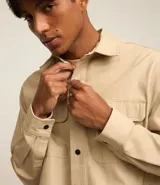 Camisa marrón de manga larga, confeccionada en sarga, con cuello inglés, abotonado delantero, bolsillos en el pecho con solapa y puños abotonados.