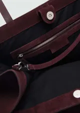 Bolso tipo shopper color bordó, confeccionado en cuero vacuno, con cierre de botón magnético, asa de hombro y bolsillo interior.