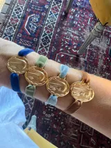 Pulsera con dije redondo dorado con la imagen de la Virgen de Fátima, sujetado por una banda elástica de terciopelo.