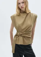 Blusa color beige con cuello perkins, sin mangas, hombreras y cinturón ajustable.