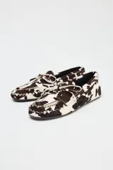 Zapato tipo mocasín en piel con pelo, con estampado animal, detalle de lazo en la parte delantera, pespunte en contraste y acabado en punta redonda.