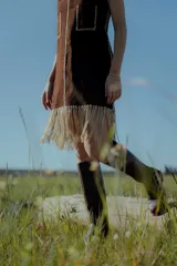 Vestido corto marrón de gamuza sintética, sin mangas, con escote en V y detalle de flecos en el ruedo. Presenta apliques bordados en el frente y laterales.