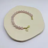 Pulsera elástica de cuentas de cuarzo rosa de 8mm con separadores de hilo rosa. Cierre de mosquetón dorado con dije de estrella con incrustaciones.