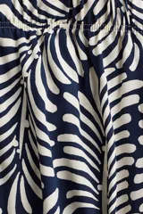 Pantalón tobillero cropped de viscosa con estampado de hojas en color crema sobre fondo azul marino. Tiene tiro alto con elástico en la cintura, bolsillos laterales y piernas amplias rectas.