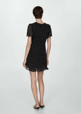 Vestido corto negro con estampado de lunares blancos, escote en V con lazo, mangas cortas y falda con volantes.