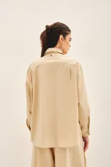 Camisa beige de poplin amplia, con botones laterales para abotonar de forma cruzada.