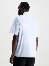 Camisa celeste de popelín de algodón superelástico, con cuello en punta, manga corta, tapeta con botones y logo con monograma de Calvin Klein en el pecho.