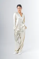 Pijama de satén color crema con detalles de puntilla en el escote, puños y ruedo del pantalón. Compuesto por camisa de manga larga con botones y pantalón recto con bolsillos laterales y elástico en la cintura.