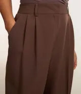 Pantalón largo de vestir color marrón chocolate, de corte sastrero con pliegues en la parte delantera y trabillas en la cintura. Confeccionado en poliéster y elastano.
