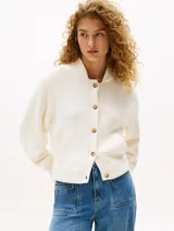 Cárdigan color crema de punto de algodón, con cuello redondo, cierre frontal con botones marrones, mangas globo, dos bolsillos delanteros y logo metálico en la manga.