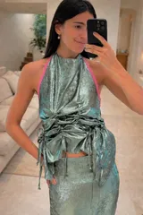 Top con escote halter, color verde agua con brillo, con un vivo a contratono rosa. Presenta jaretas en el frente para aportar textura y volumen. La espalda queda abierta y se ajusta con tiras para anudar.