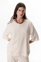 Blusa de lino color beige claro, con mangas 3/4 y cuello redondo. Presenta pespuntes a contratono en el centro, puños y ruedo.