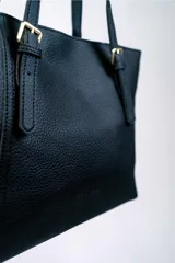 Cartera tipo shopper color negro, con textura símil cuero, doble asa de hombro con hebillas doradas y cierre superior.