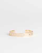 Brazalete dorado de metal con la palabra "Lovely" calada y pequeños corazones troquelados.