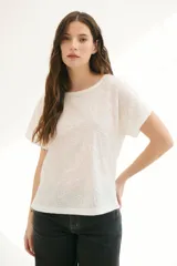 Blusa blanca con estampado de hojas en relieve, cuello redondo y mangas cortas.
