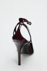 Zapato de tacón destalonado color borgoña, con efecto acharolado, tacón fino, cierre mediante hebilla en la pulsera al tobillo y acabado en punta.