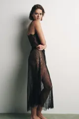Vestido largo semitransparente de encaje negro, con escote en pico, tirantes finos dobles, abertura en la espalda y cierre con botones ocultos.