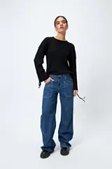 Sweater negro de punto canalé con detalle de trenzado en las mangas y lazo ajustable en el ruedo.