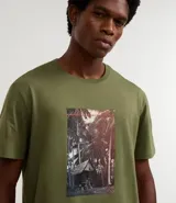 Remera verde oliva de algodón, corte comfort, con cuello redondo y mangas cortas. Estampa rectangular con paisaje de cabaña en la playa.