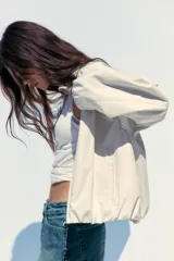 Chaqueta bomber color crudo con cuello solapa, manga larga con puño elástico interior, bolsillos laterales, forro interior, bajo acabado en elástico y cierre frontal con cremallera.