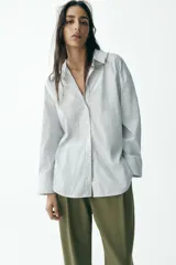 Camisa blanca con rayas verticales azul marino y lurex plateado, de corte recto, cuello solapa, escote en pico y cierre frontal con botones.