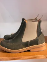 Bota Chelsea color verde oliva, con elásticos laterales en color beige, suela plana de goma color caramelo y tirador trasero.