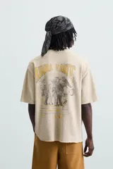 Camiseta color beige de punto tejido en hilatura de algodón, corte relaxed fit, cuello redondo y manga corta. Estampación con efecto lavado combinada a contraste en espalda. Acabados irregulares.