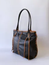 Bolso tipo tote de cuero negro con costuras a la vista en color camel. Tiene doble asa de hombro y está forrada en tela.
