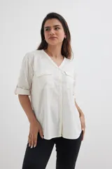 Camisa color crema de algodón con escote en V, mangas 3/4 con trabilla y dos bolsillos con solapa en el pecho.
