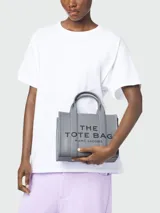 Bolso tote pequeño de cuero color negro, con doble asa corta y correa lateral. Estampado frontal con el nombre de la marca y el tipo de bolso.