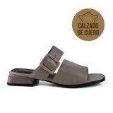 Sandalia de cuero color visón, con tira ancha sobre el empeine y tira con hebilla ajustable en el tobillo. Tiene taco bajo cuadrado y suela de goma.