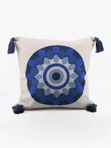 Funda de almohadón cuadrada color crudo con estampado circular concéntrico en tonos de azul y borlas decorativas en las esquinas.