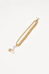 Pulsera dorada de doble cadena con cierre de barra en forma de aro. Incluye una perla colgante y un dije con la forma de una cara.