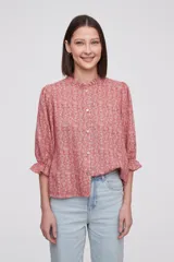 Blusa estampada con flores azules y hojas verdes, cuello mao con volados, mangas 3/4 con volados en los puños y cierre frontal con botones.