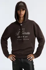 Sudadera marrón con capucha ajustable con cordones y bordado blanco con el texto 'ZAFA A Coruña Established 1975 Rúa Juan Flórez 64-66'.