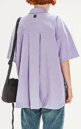 Camisa de manga corta color lavanda con doble bolsillo y ojal delantero con solapa en uno de ellos. Tiene calce oversize y está realizada en tejido plano suave al tacto.