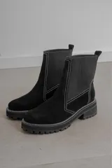 Bota corta negra de gamuza y neopreno, con elástico lateral y costuras blancas. Tiene suela track y tirador trasero.