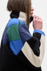 Campera con cierre frontal y cuello alto, confeccionada en fleece color crudo, con paneles en rojo, marrón y bordó.