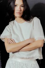 Blusa color crudo de lino con mangas cortas y detalle de flecos en el ruedo y las mangas. Cierre con botón en la espalda.