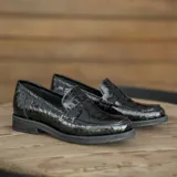Mocasín de cuero vacuno en color negro, con taco de madera foliado y diseño de punta redonda.